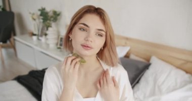 Evde bakım kavramı. Yenilenme için yüz tedavisi uygulaması. Yüz bakımı ve güzellik ayinleri. Evde güzellik tedavisi. Kadın anti-reşit yüz masajı için gua sha yeşim kazıyıcı kullanıyor..