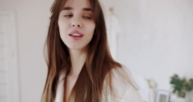 Yüzü sağlıklı cilt masajı elleriyle beyaz bornozlu güzel kadın yüzüne dokunuyor. Mükemmel sağlıklı tenli bir kadın elleriyle yüzüne dokunuyor. ev güzelliği kavramı.