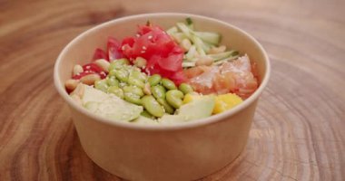 Poke kasesi, geleneksel Hawaii çiğ balık salatası. Organik ve temiz yemek. Japon yemeği, somon, pirinç, avokado, edamame fasulyesi, ahşap arka planda salatalık..