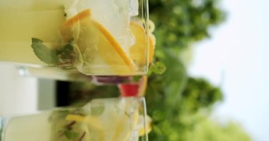 Limon, narenciye, portakal, greyfurt, nane, su ve buz ile ferahlatıcı limonata içeceği, doğal arka planda dönen limonata bardakları. Hikayeler için dikey video.
