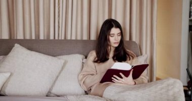 Woman relaxing in bed and reading a book in the bedroom in the modern house. A beautiful woman is resting and relaxing at home in a cozy bedroom. Time for relax and education concepts.