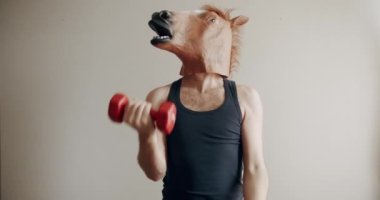 At maskeli komik bir adam evde beyaz arka planda el eğitimi için ağırlık egzersizi yapıyor. Evde komik bir spor salonu var. Komik Sağlık ve Spor Konsepti. Esprili esnemeler..