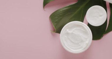 Kozmetik ürünleri için beyaz kavanozlar ve yüz silindiri. Stüdyoda pembe arka planda Monstera yapraklı. Doğal malzemelere dayalı kozmetik yağları, cilt bakımı için doğal kozmetik ürünleri.