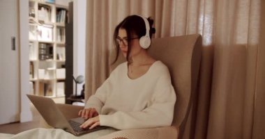 Güzel Genç Kadın, dizüstü bilgisayarda çalışırken sandalyede oturuyor. Defterde Kazak Giyen Şehvetli Kız. Çalışmalar, İnternet Sörfleri, Konforlu Daire 'de dinlenirken Sosyal Medya Kullanımı