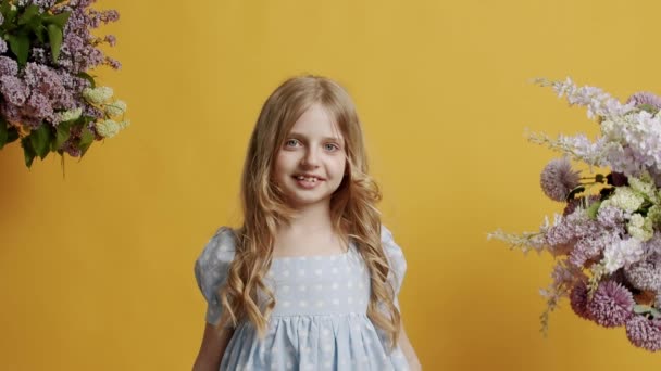 7歳の少女は明るいブルーのドレスを着ており スタジオの黄色の背景の部屋を美しく見ています カメラを見て優しい笑顔の美しい女の子 — ストック動画