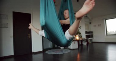 Hafif stüdyodaki yoga seansı sırasında havadan hamakta baş aşağı asılı güçlü bir erkek resmi. Sınıfta çalışıyor, aero yogası yapıyor. Spor etkinliği.
