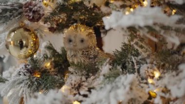 Karlı dalları, altın topları, sevimli baykuşu ve ışıldayan çelengi olan Noel ağacına yakın çekim. Noel ağacı ve sıcacık bir evde yeni yıl süsü. Dekorasyon fikri