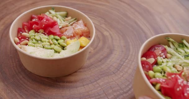 平底锅 配上鲑鱼 黄瓜和西红柿 木制背景 女性手上的高角镜把带有夏威夷菜的纸碗放在桌上 健康的食物 — 图库视频影像