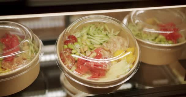 有鲑鱼 芝麻豆和西红柿的平底锅在咖啡店里陈列 寿司碗与鱼 生菜和腌制生姜在一次性包装 拿走概念 健康饮食 — 图库视频影像