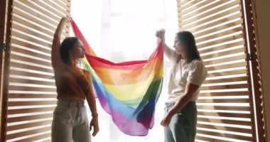 İki mutlu kadın lezbiyen kucaklaması ve lgbtq gökkuşağı bayrağı sallayarak gurur ayını kutluyorlar. Gülümseyen kadın çift birlikte vakit geçiriyor. lgbt toplumunu destekleme kavramı