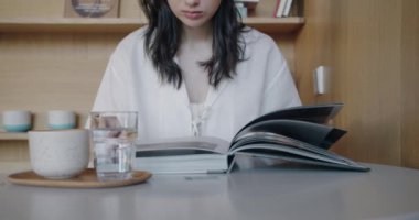 Kafe masasında bir fincan kahve içip kitap okuyan genç bir kadın. Kadın müşteri rahat bir restoranda kahvaltı yapıyor. Yaşam tarzı kavramı