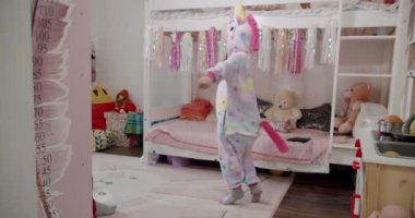 Tek boynuzlu at kostümlü mutlu bir kız çocuğu. Eğlenin ve festival dekoru ve oyuncaklarıyla dans edin. Komik pijamalı neşeli çocuk evde dönüp duruyor. Çocukluk kavramı