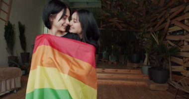 Birbirine aşık iki lezbiyen kız, sarılıyor ve gökkuşağı bayrağına sarılmış. Birbirlerine şefkatle sarılan gülümseyen kadın çift. Lgbt kavramı