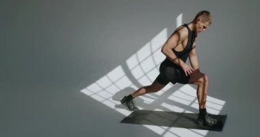 Genç atletik adam vücut çalışmaya ve ısınma egzersizleri yapmaya hazırlanıyor. Kaslı erkek, beyaz arkaplan ile stüdyoda yoga minderinin üzerinde geriniyor.