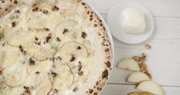 モッツァレラ パルメザン ゴルゴンゾーラを備えた新鮮なピザフォルムジグのトップビューは 回転スタンドで提供されました イタリアのおいしいピザ テーブル上の食材の近くのプレートに真珠とクルミのチーズ — ストック動画