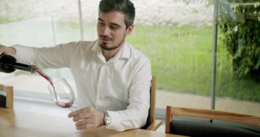 Erkek sommelier kırmızı şarabı tatmak ve şişeden havalandırıcıya su dökmek ister. Beyaz gömlekli bir erkek masada oturuyor ve alkol şarabı içiyor.