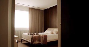 Modern iç mimarisi olan bir otel odası, ortopedik yataklı, yastıklı ve ekoseli rahat bir çift kişilik yatak. Lüks yatak odası, ahşap mobilyalar, yatak odası ve perdeli pencere. Rahat uyku konsepti