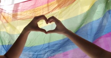 Lezbiyen kadınların ellerinde LGBTQ gökkuşağı arka planında kalp sembolü görülüyor. Homoseksüel topluluğun desteği, cinsel ve aşk çeşitliliği. LGBT gurur ayı konsepti