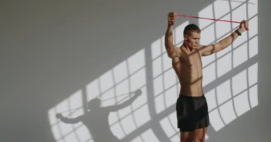 Atletik adam egzersiz yapıyor ve beyaz arka planlı bir stüdyoda direniş bandıyla egzersiz yapıyor. Üstsüz erkek, mükemmel vücut eğitimi omuzları ve spor aletleri kullanan sırt kasları var..