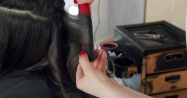 Moda saç stili yaratan kuaförün el kamerası görüntüsü. Kadın kuaför, güzellik stüdyosunda saç maşası kullanarak genç müşteriyi tıraş ediyor. Kuaförde kuaför yaratmak.