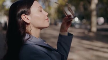 Çekici kadın güneş gözlüğü taktı ve caddede kameraya baktı. Güneşli bir günde gözlüklü şık bir kadının portresi..