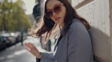 Modayı takip eden güneş gözlüklü genç ve çekici bir kadın şehrin dışındaki duvarlara yaslanırken kameraya poz veriyor. Sokakta şık giyinmiş kadın portresi