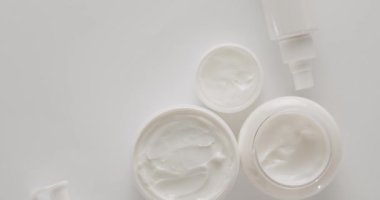 Beyaz kavanozlar ve kozmetik tüpleri stüdyoda beyaz bir arka planda dönüyor. Doğal malzemelere dayalı kozmetik yağları, fırça, serum, tonik, vücut bakımı, cilt bakımı. Farklı kozmetik şişeleri grubu.