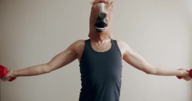 At maskeli komik bir adam evde beyaz arka planda el eğitimi için ağırlık egzersizi yapıyor. Evde komik bir spor salonu var. Esprili esnemeler. Komik ev egzersizi.