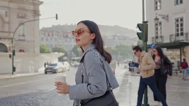 スタイリッシュな衣装とトレンディなサングラスを着た若い女性は 歩行者の散歩道の道路を渡って仕事に行きます ビジネス女性はコーヒーのカップと街の通りを歩きます — ストック動画
