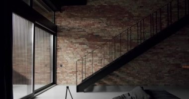 Siyah merdivenli, geniş pencereli, minimalist, tuğla duvarlı bir oturma odası. Çatı katının modern iç mekanı. Tuğla oda, iç yapı, merdivenli tuğla duvar arka planı..