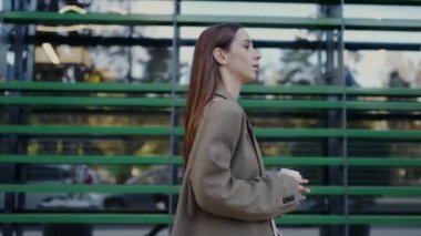 Çekici, başarılı, şık elbiseli bir kadın bir fincan kahve alıp işe gidiyor. Kentin caddesinde yürüyen kendine güvenen genç bir iş kadını.