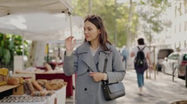 Trençkotlu, çantalı şık bir kadın şehirdeki pazar fuarında yürüyor. Pazar yerinde genç bayan aksesuarları.