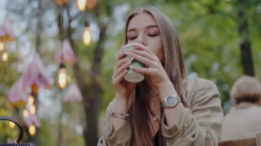 Caddedeki kafede oturan ve taze kahve içen genç ve güzel bir kadın. Kadın molada dışarıda, parkta sıcak çay içiyor.