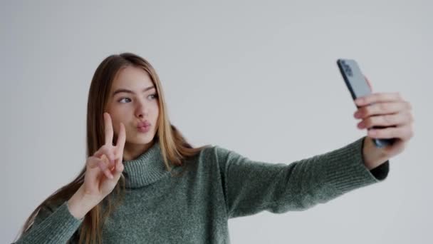 Νεαρή Ελκυστική Γυναίκα Κατέχει Smartphone Και Δείχνει Χειρονομία Ειρήνης Ενώ — Αρχείο Βίντεο