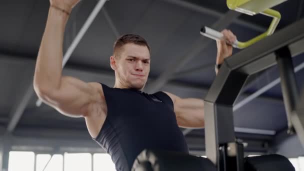 男性は筋肉をポンプするフィットネスセンターのシミュレーターで訓練します ハンサムは運動をするスポーティな男に合います 屋内フィットネスセンターの新しいシミュレーターで筋肉運動選手のトレーニング 強力なトレーナー — ストック動画