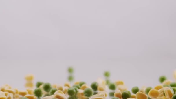 多くの熟した緑のエンドウ豆とトウモロコシの穀物は 孤立した白い背景の反射面に転がります 新鮮な緑のエンドウ豆とトウモロコシの穀物を閉じます 新鮮な緑のエンドウ豆と白の背景にトウモロコシ — ストック動画