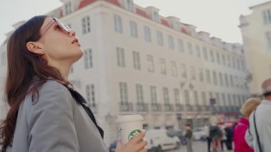 Elinde bir fincan kahveyle caddede dikilen bir kadını gösteren bir video. Sokakta dikilen Kadın Kahve fincanı