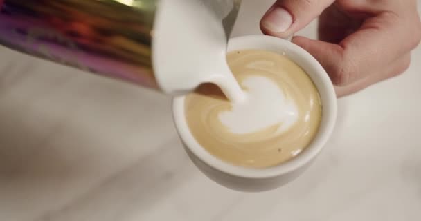 バリスタはカプチーノを作り ミルクを冷凍して心臓の形をした飲み物に注ぎます ラテアートコンセプト コーヒーショップで新鮮なカフェインドリンクを準備する男性のクロップビュー — ストック動画