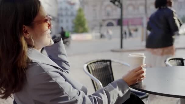 若い女性は 屋外の街のカフェでコーヒーを飲みながら 早朝の静けさを楽しみます 朝の時間に街の屋外カフェでコーヒーでリラックスする女性 — ストック動画