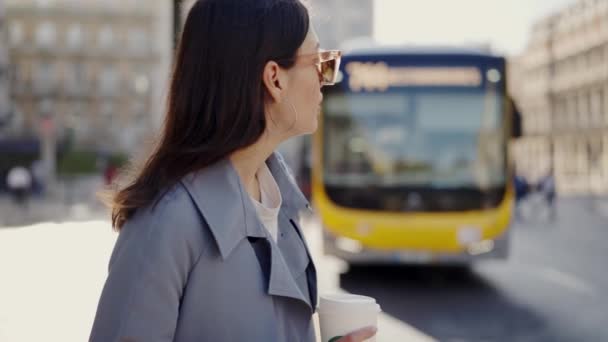 コーヒーを飲みながらバスの前に立っている女性を撮影したビデオ バス前でコーヒーを飲む女性 — ストック動画