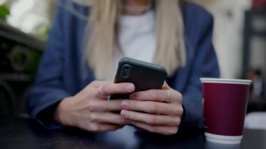 Akıllı telefon kullanan ve kafe masasında otururken mesaj gönderen bir kadın. Kadın cep telefonunun el ele tutuşması ve çevrimiçi sohbet görüntüsü.