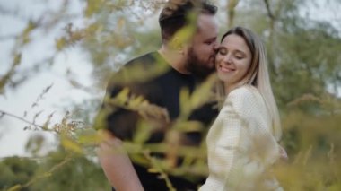 Mutlu kadın ve erkek çift parkta birlikte yürüyor, sarılıyor ve öpüşüyorlar. Neşeli erkek ve kadın aşıklar, birlikte vakit geçiriyorlar, eğleniyorlar ve doğada dinlenirken gülüyorlar.