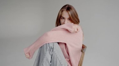 Sıcak pembe kazaklı güzel bir kadın model. Sandalyeye oturmuş ve beyaz arka planlı bir stüdyoda kameraya poz veriyor. Genç ve güzel bir kadının portresi.