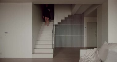 Çıplak ayaklı bir kadın modern evdeki oturma odasına iniyor. Kapalı kapılar ardında merdivenleri olan şık bir daire..