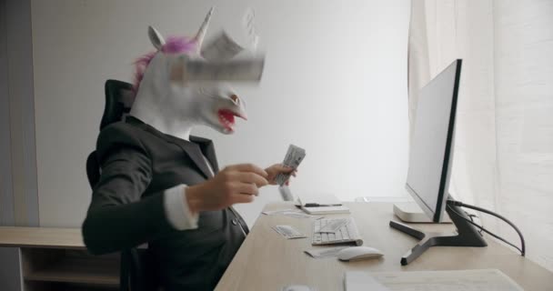一个戴着独角兽面具 身穿西装的有趣男人 享受着他的经济成功 并在办公室数钱 戴独角兽面具的商人在数着堆积如山的现金美元利润工资 — 图库视频影像