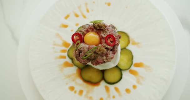 真っ白な背景に大きなプレートにソースと赤と緑のチリコショウと一緒に美しく配置された生の卵黄で調理された肉 レストランフード トップビュー — ストック動画