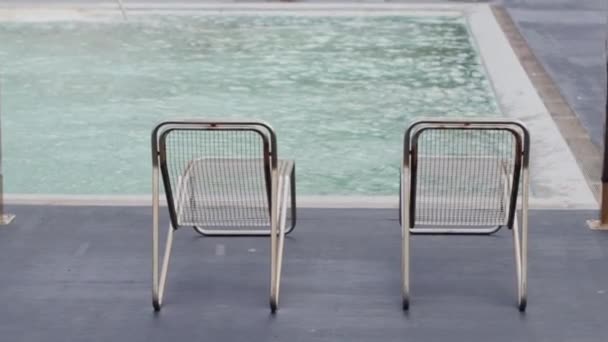 屋外プール近くの空の金属チェイスラウンジ 夏季に自然に囲まれた休息とリラクゼーションのための座席 — ストック動画