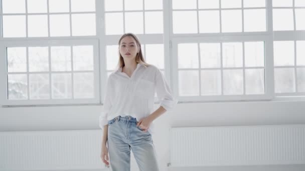 Kvinna Vit Skjorta Och Jeans Står Framför Ett Träinramat Fönster — Stockvideo