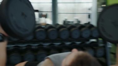 Genç atletik adam spor salonunda çalışıyor ve dambıllarla antrenman yapıyor. Spor malzemelerini kullanarak spor merkezinde egzersiz yapan kaslı erkek vücut geliştirici..