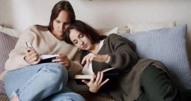 İki kadın lezbiyen kanepede uzanıp ilginç kitaplar okuyorlar. Genç bayan çift hafta sonu evde dinleniyor.. 